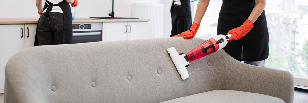 Reinigungskraft saugt ein graues Sofa mit Handsauger – gründliche und regelmäßige Unterhaltsreinigung für saubere Wohnräume