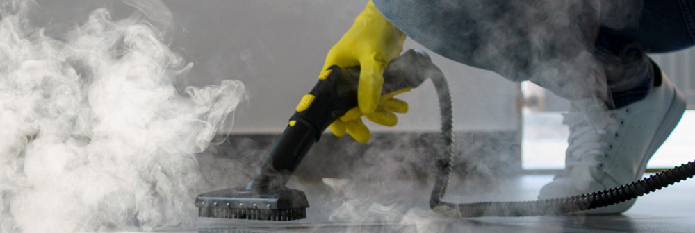 Reinigungskraft mit Dampfreiniger und gelben Handschuhen reinigt Boden – intensive Grundreinigung für hartnäckigen Schmutz